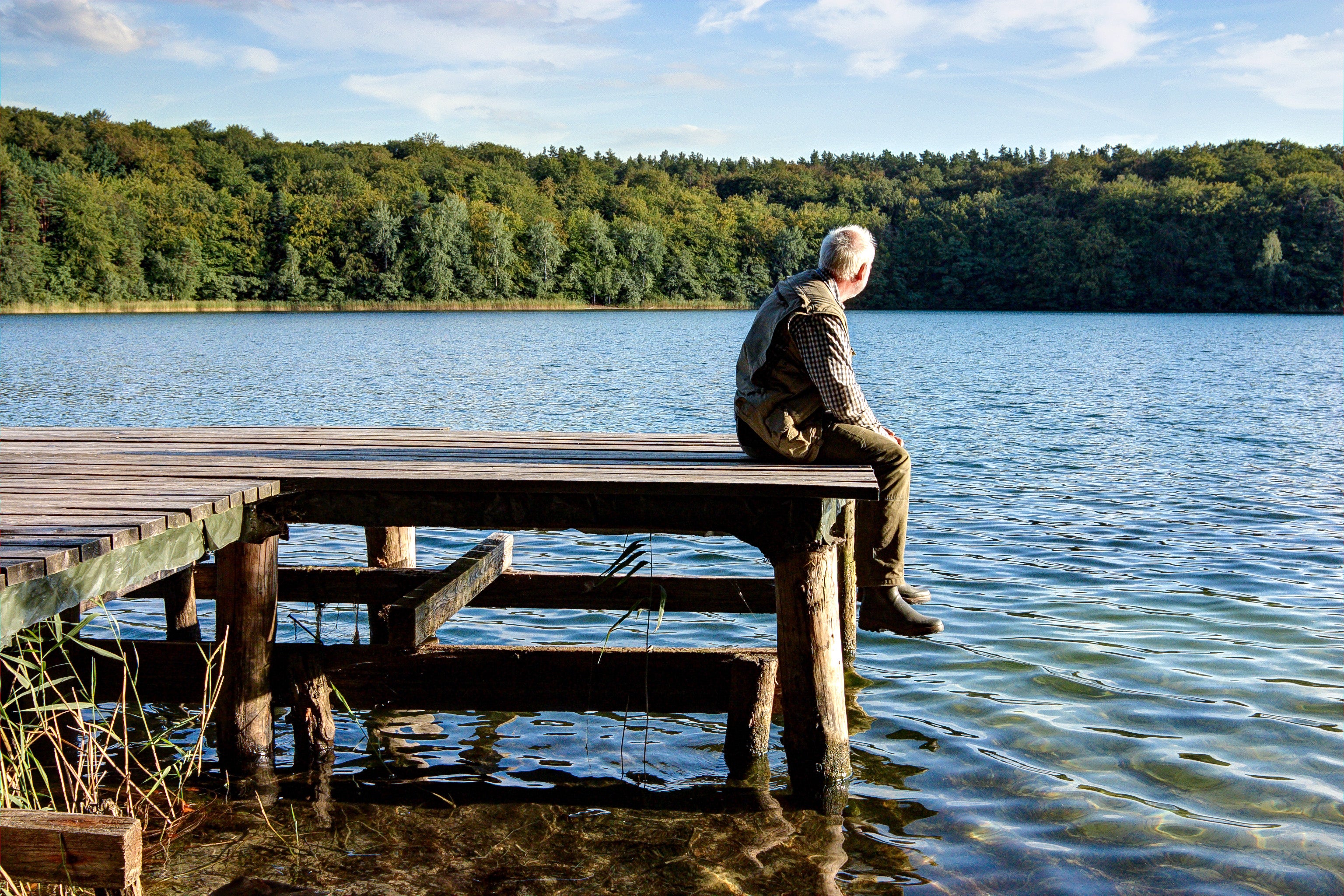 Äldre man sitter på brygga vid en sjö