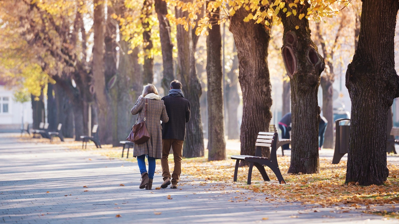 Medelålders par vandrar bland höstlöv i park