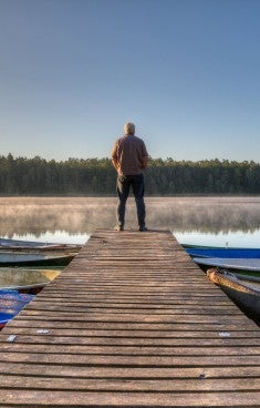 Äldre man stå längst ut på en brygga och tittar ut över sjön