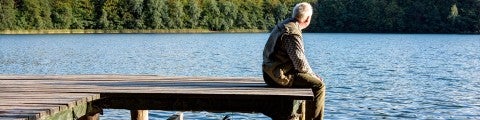 Äldre man sitter på brygga vid en sjö